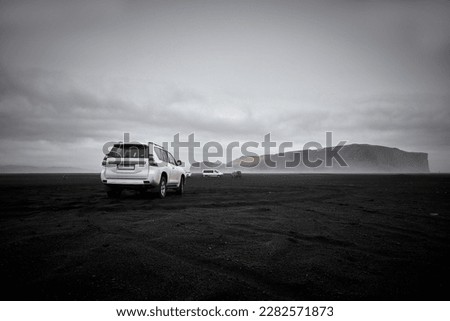 An SUV Is Parked On The Famous Black Sand Beach, With A Mountain In TheBackground in The Distance
