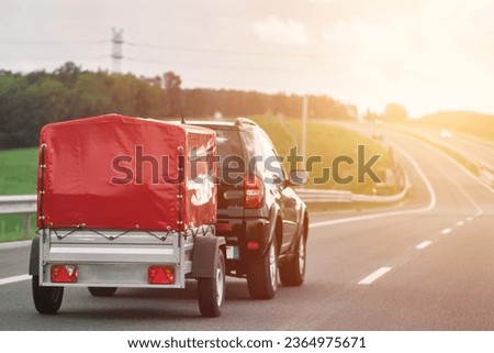 SUV with trailer goes on the highway. Moving stuff with a small rentable trailer.