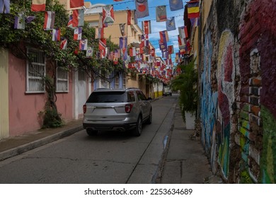 SUV truck driving through a small narrow street decorated with many different countries flags. - Shutterstock ID 2253634689