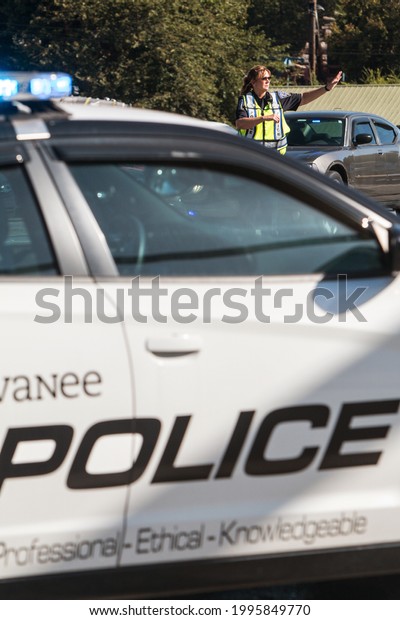 Suwanee, GA  USA - September 21, 2019:  A female\
police officer directs vehicular traffic at Suwanee Fest, as blue\
lights flash on her police car, on September 21, 2019 in Suwanee,\
GA.