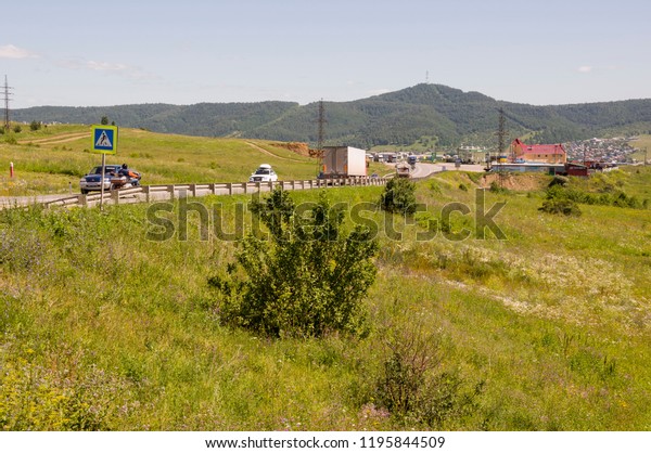 Sverdlovsk\
region, Ural, Russia. September 1, 2018. Asphalt road going across\
mountains and green forests. Trees and their shadows on the grass.\
Sunny summer day with blue sky. Ural\
landscape