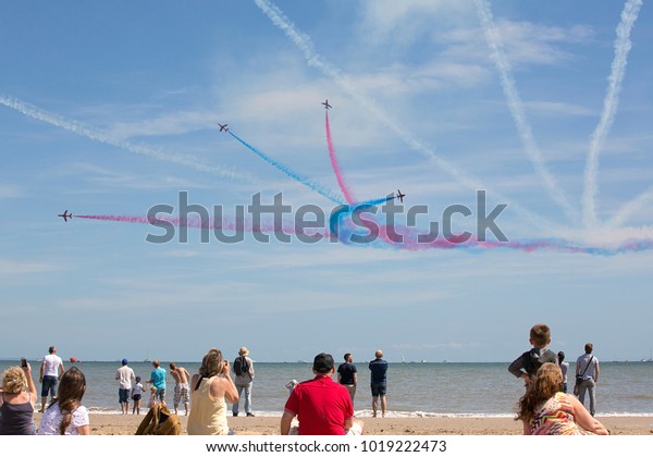 Swansea, UK: July 07, 2017: An aerobatic display\
team perform for the delighted crowds on Swansea beach. Families\
and spectators watch the coloured smoke trails at the annual free\
event.