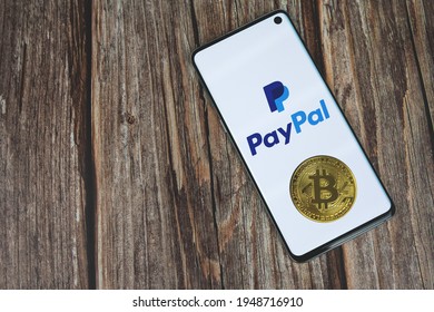 SWANSEA, UK - MARCH 31, 2021: PayPal Logo On Phone Screen With Bitcoin Cryptocurrency Coin On Wooden Background With Copy Space. Checkout With Crypto Concept