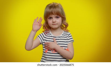 I Swear To Be Honest. Responsible Sincere Little Kid Child In Shirt Raising Hand To Take Oath, Promising To Be Honest And To Tell Truth, Keeping Hand On Chest On Yellow Wall. Children Girl Emotions