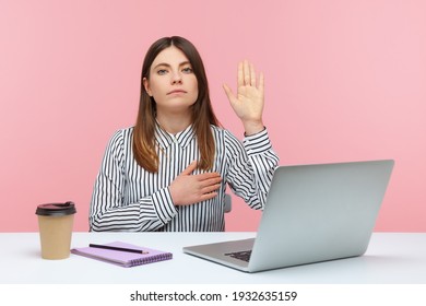 I swear! Honest dedicated woman office worker raising hand to give promise sitting at workplace, taking oath with trustworthy faithful expression. Indoor studio shot isolated on pink background