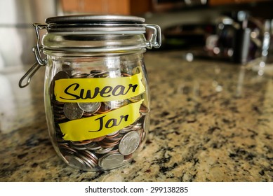 Swear Jar. A clear glass jar filed with coins and bills, saving money. The words "Swear Jar" written on the outside.