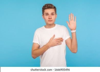 I swear! Portrait of honest sincere man in t-shirt giving promise with hand on heart, pledging allegiance, giving vow with responsible serious face. indoor studio shot isolated on blue background