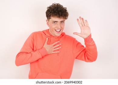 I Swear, Promise You Not Regret. Portrait Of Sincere Young Caucasian Man With Curly Hair Wearing Sweatshirt ​white Background Raising One Arm And Hold Hand On Heart As Give Oath, Telling Truth, Want 