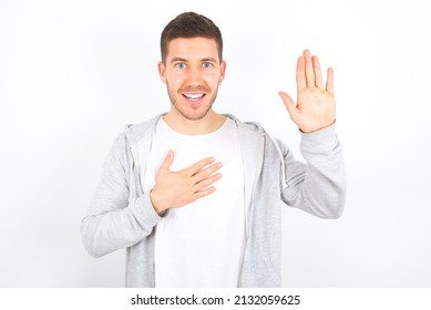 I Swear, Promise You Not Regret. Portrait Of Sincere Young Caucasian Man Wearing Casual Clothes Over White Background Raising One Arm And Hold Hand On Heart As Give Oath, Telling Truth,