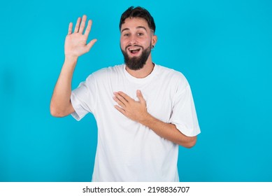 I Swear, Promise You Not Regret. Portrait Of Sincere Bearded Caucasian Man Wearing White T-shirt Over Blue Background Raising One Arm And Hold Hand On Heart As Give Oath, Telling Truth, Want You To Be