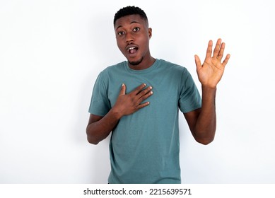 I Swear, Promise You Not Regret. Portrait Of Sincere Young Handsome Man Wearing Green T-shirt Over White Background Raising One Arm And Hold Hand On Heart As Give Oath, Telling Truth, Want You 