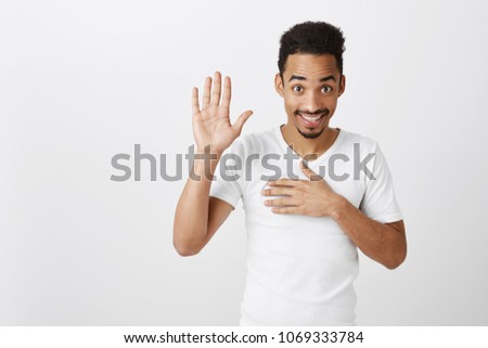 Swear to say truth. Studio shot of sincere happy african-american male with afro haircut, raising palm and holding hand on chest, promising to me honest, standing over gray background