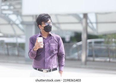 Sweating Asian Young Businessman With Surgical Face Mask Using Mobile Phone During Office Hours As Part Of Business New Normal