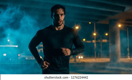 Sweating Tired Athletic Muscular Young Man in Sports Outfit Jogging in a Street Filled With Smoke. He is Running in an Evening Urban Environment Under a bridge. - Powered by Shutterstock