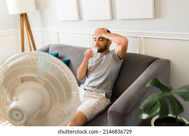 Sweaty man feeling very hot because of a heat stroke. Latin man sweating and drinking a lemonade with the fan on