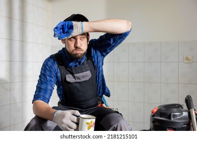 A Sweaty Man Tired Of Construction Work Sits In A Renovated Room On A Stool Wipes His Forehead With A Dirty Glove With A Sigh Sips Water From A Mug, Coffee.