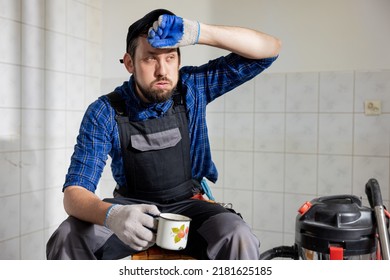 A Sweaty Man Tired Of Construction Work Sits In A Renovated Room On A Stool Wipes His Forehead With A Dirty Glove With A Sigh Sips Water From A Mug, Coffee.