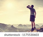 Sweaty thirsty runner at the end of path drinking from transparent bottle. Wild hilly landscape.  Man in shorts and white dress