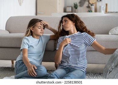 Sweaty tired woman sits on floor next to sofa and fan looking back at teenage daughter after coming back from summer city walk. Exhausted relaxed teen girl enjoys cold wind in hot sunny weather - Shutterstock ID 2258138501