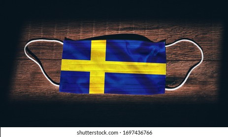 Sweden National Flag At Medical, Surgical, Protection Mask On Black Wooden Background. Coronavirus Covid–19, Prevent Infection, Illness Or Flu. State Of Emergency, Lockdown