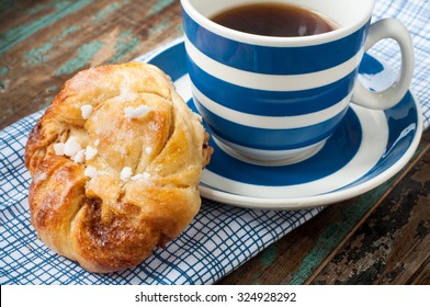 Swedish Cinnamon Berry Bun Served On A Rustic Wooden Table With A Cup Of Freshly Brewed Coffee In A Blue And White Striped Cup And Saucer. Coffee And A Bun Is A Tradition In Sweden Known As Fika.