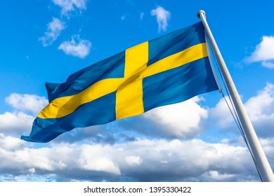 Swedish flag against blue sky with white clouds. Beautiful swedish flag seen in Stockholm. Swedish flag fluttering in wind on the ship. Sveriges nationaldag. National Day of Sweden. Swedish Flag Day.