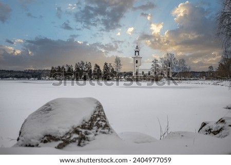 Swedish houses, small white church by a lake in a cold winter landscape with snow and ice. Vårviks kyrka in Sweden