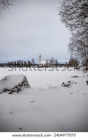 Swedish houses, small white church by a lake in a cold winter landscape with snow and ice. Vårviks kyrka in Sweden