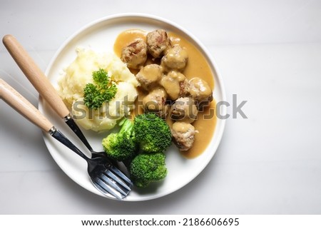Swedish Meatball with brown mushroom sauce. Served on ceramic plate, on white table.