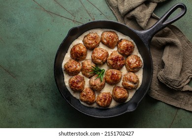 Swedish Meatballs made with ground meat, onion, egg, bread crumbs and nutmeg. With creamy gravy in black pan skillet.  On green concrete table.