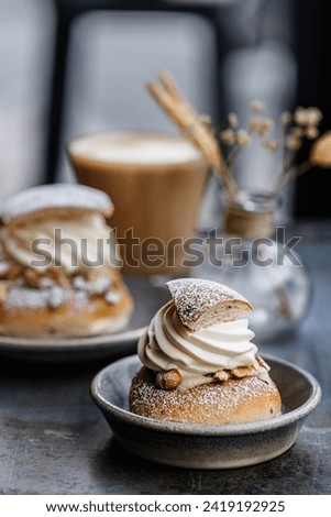 Swedish Semla buns with whipped cream and chopped almond. Two wheat flour buns, flavoured with cardamom and filled with almond paste. Coffee glas in the background and a small vase with dried flowers.