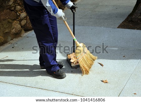 Sweeper, municipal cleaning worker sweeping the autumn leaves on the city sidewalk
