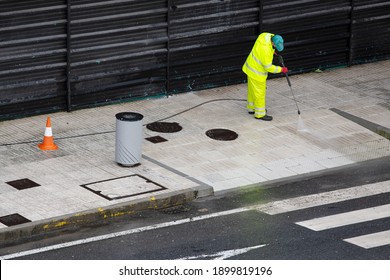 Sweeper Worker Cleaning A Street Sidewalk With High Pressure Water Jet Machine On Rainy Day. Copy Space