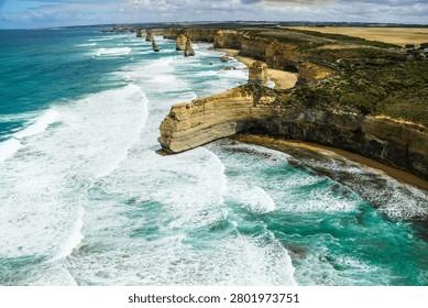 A sweeping aerial view of limestone cliffs, surf, and sea stacks along the Twelve Apostles coastline.