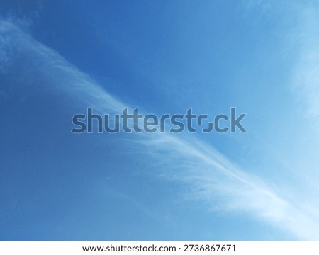 A sweeping diagonal of cirrus clouds cuts across the sky, forming a fluid pattern under natural lighting. The scene conveys graceful motion and atmospheric clarity in a minimalist tone.