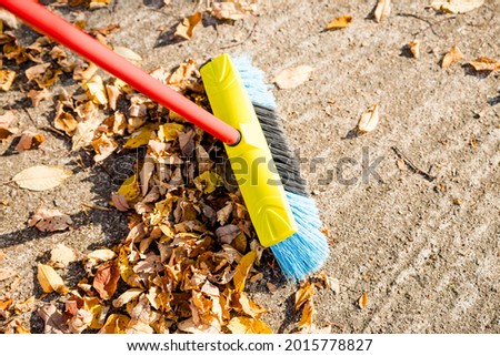 Sweeping the fallen leaves from the garden ground for recycling during autumn fall season.Man brooming the street to collect dry fallen leaves.