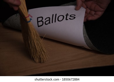 Sweeping Hand Broom Showing Movement Toward A Rug Or Carpet Where The Word Ballot Is Being Swept Under The Carpet Rug. Brown Table Top And Green Rug With White Paper With Black Word Ballot Printed