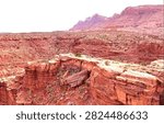 Sweeping high-angle view of vast layered red sandstone canyons and rugged mesas stretching across Utah’s iconic American Southwest desert. Ancient horizontal rock strata in rich rust and terracotta hues form jagged cliffs and flat-topped ledges, dotted with hardy desert shrubs and small pines. Massive distant mountain ridges rise under a soft pale sky, capturing the raw geological grandeur, timeless beauty, and immense scale of the Colorado Plateau’s legendary red rock wilderness.