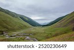 A sweeping view of a verdant valley nestled between rolling hills under a cloudy sky in the Scottish Highlands.