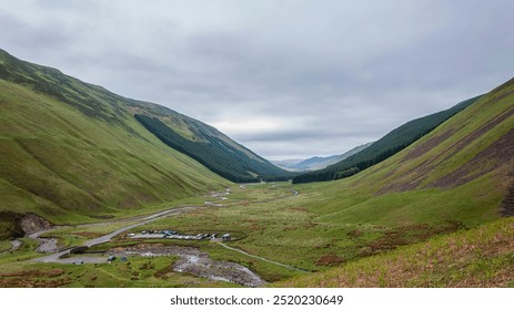 A sweeping view of a verdant valley nestled between rolling hills under a cloudy sky in the Scottish Highlands. - Powered by Shutterstock