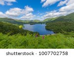 Sweeping vista of Lake Grasmere in the Lake District, UK on a sunny spring day.  Blue sky with puffy white clouds and foxglove flowers in the foreground.