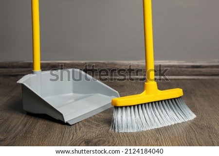 Sweeping wooden floor with plastic broom and dustpan indoors
