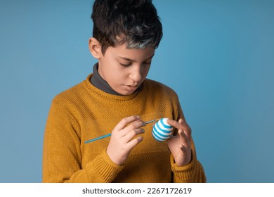 Sweet 10  year  old caucasian boy painting white Easter egg and paintbrush blue background  Great for Easter  themed designs illustrating children's crafts   activities