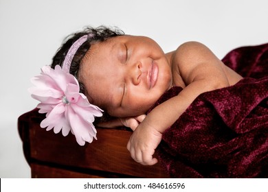 A sweet African American baby sleeps in a wooden box.  She has a small smile on her lips.