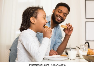 Sweet African American Girl And Her Dad Eating Cookies At Kitchen, drinking milk, side view