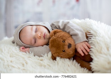 Sweet baby boy in bear overall, sleeping in bed with teddy bear stuffed toys, winter landscape behind him