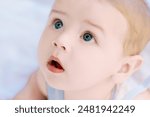 Sweet baby boy with big blue eyes lies on his back in a blue and white outfit. Looking up with an adorable expression. The portrait captures innocence and curiosity. Radiating happiness and wonder