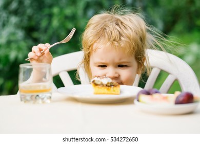 Sweet baby boy blond kid eats delicious dessert cake and drinks juice on sunny summer day on natural background