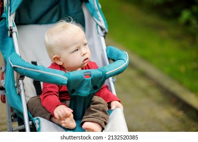 Sweet baby girl sitting in a stroller outdoors. Little child in pram. Infant kid in pushchair. Summer walks with kids. Family leisure with little child.