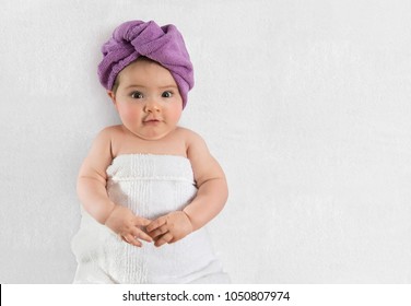 Sweet baby girl wrapped in white towel and purple bath turban